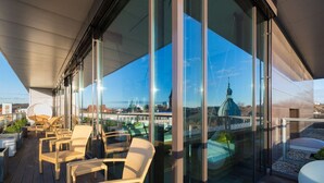 Een modern buitenverblijf met rieten stoelen en een glazen balustrade met uitzicht op een stadsgezicht.