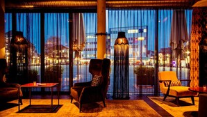 Een moderne hotelkamer met grote ramen, een vloerlamp en een uitzicht op de stad 's nachts.