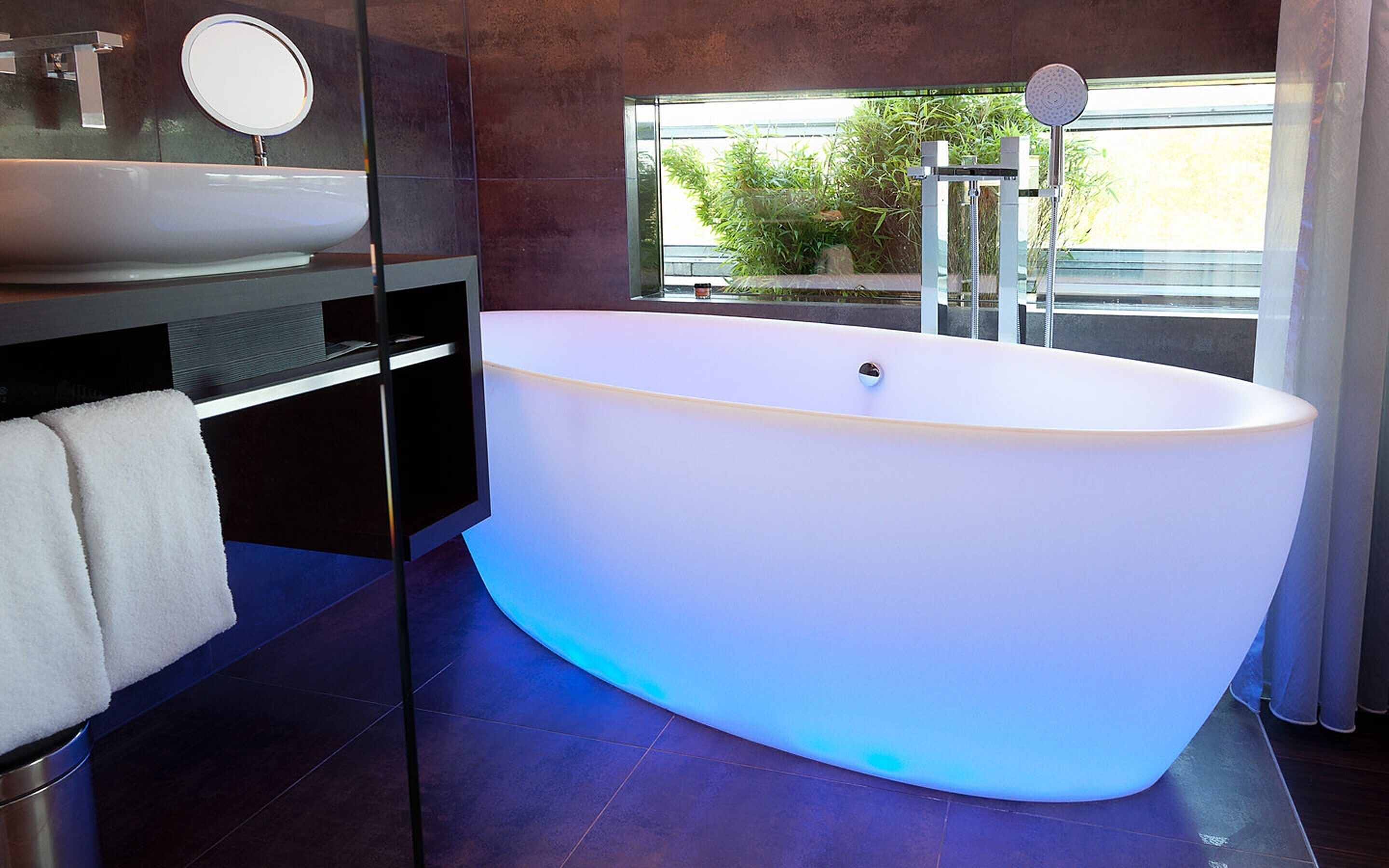 A modern bathroom with a freestanding bathtub, a round mirror, and a sink.