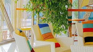 A brightly lit, modern cafe with wicker furniture, colorful cushions, and a hanging plant. - Hotel Stella Maris (Cesenatico)