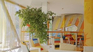 A modern interior with wicker furniture, a large plant, and colorful wall art. - Hotel Stella Maris (Cesenatico)
