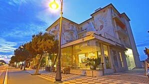 A hotel with a glass facade, outdoor seating, and a checkered pavement. - Hotel Stella Maris (Cesenatico)