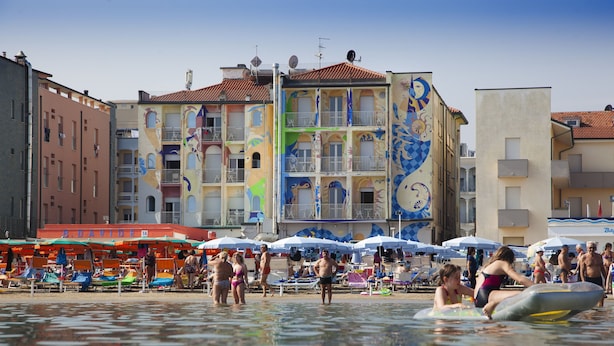 A beach with colorful buildings in the background and people enjoying the water. - Hotel Stella Maris (Cesenatico)