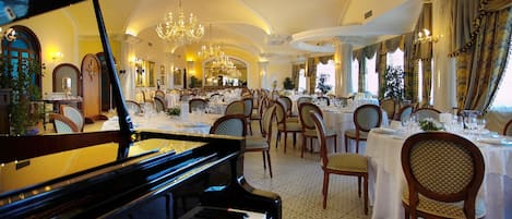 Un gran salón comedor con un piano de cola, elegantes candelabros y una decoración ornamentada.