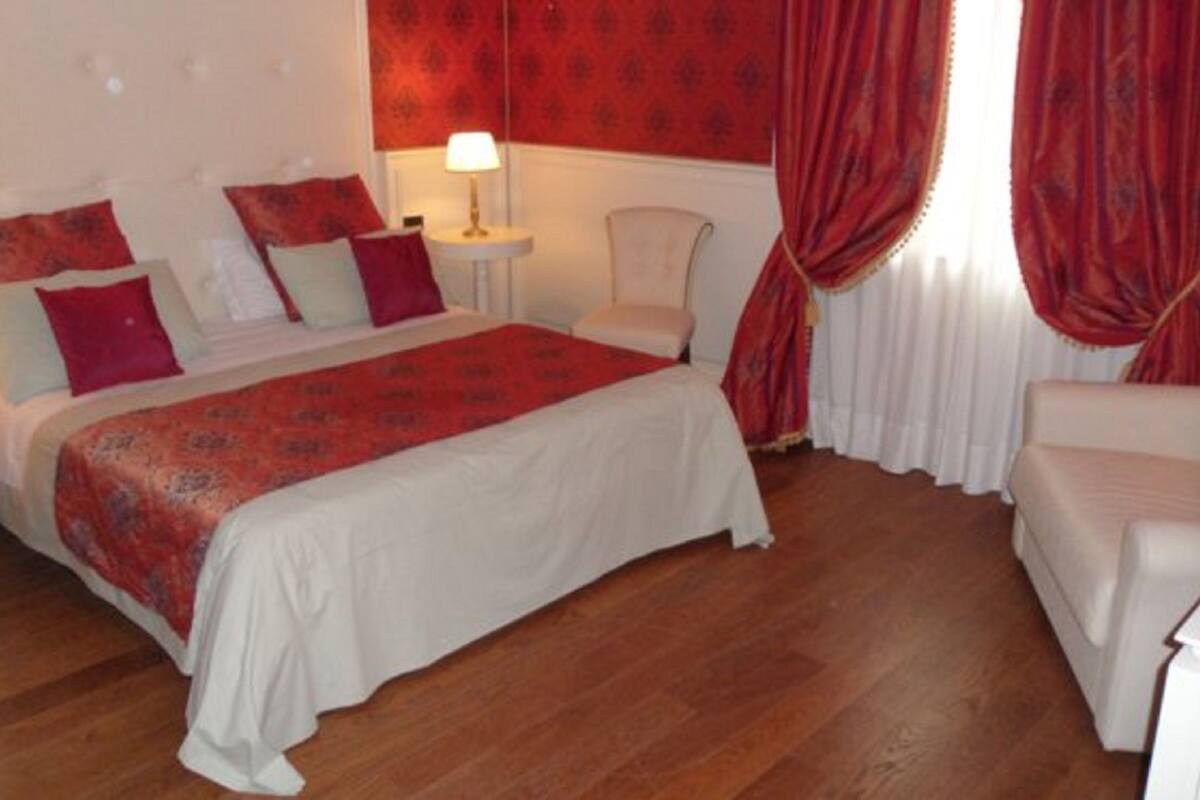 A hotel room with a bed, a chair, a nightstand, and a window with curtains.