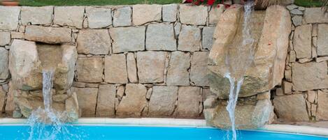 A stone wall with a pool and water features.