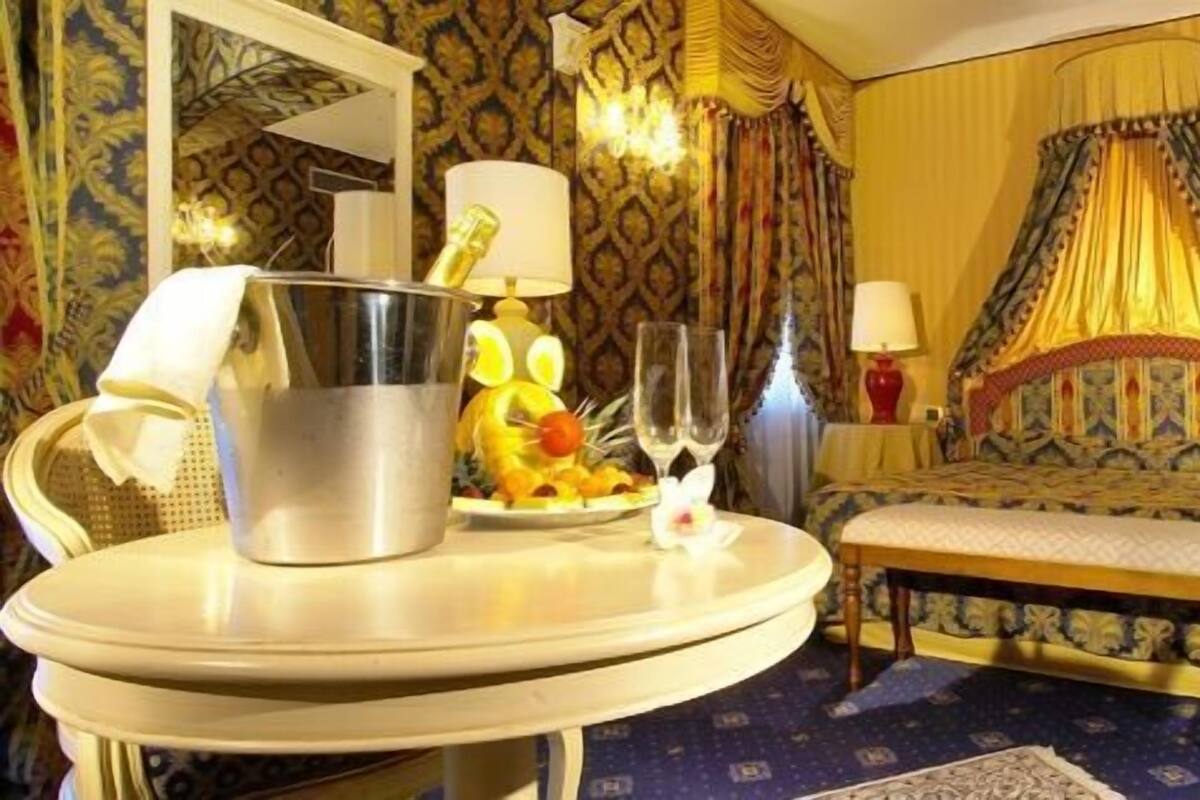 A hotel room with a bed, a round table with a lamp, a chair, and a bedside table with a lamp.