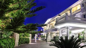 Een hotel met een gebogen balkon, stenen zuilen en weelderige begroeiing.