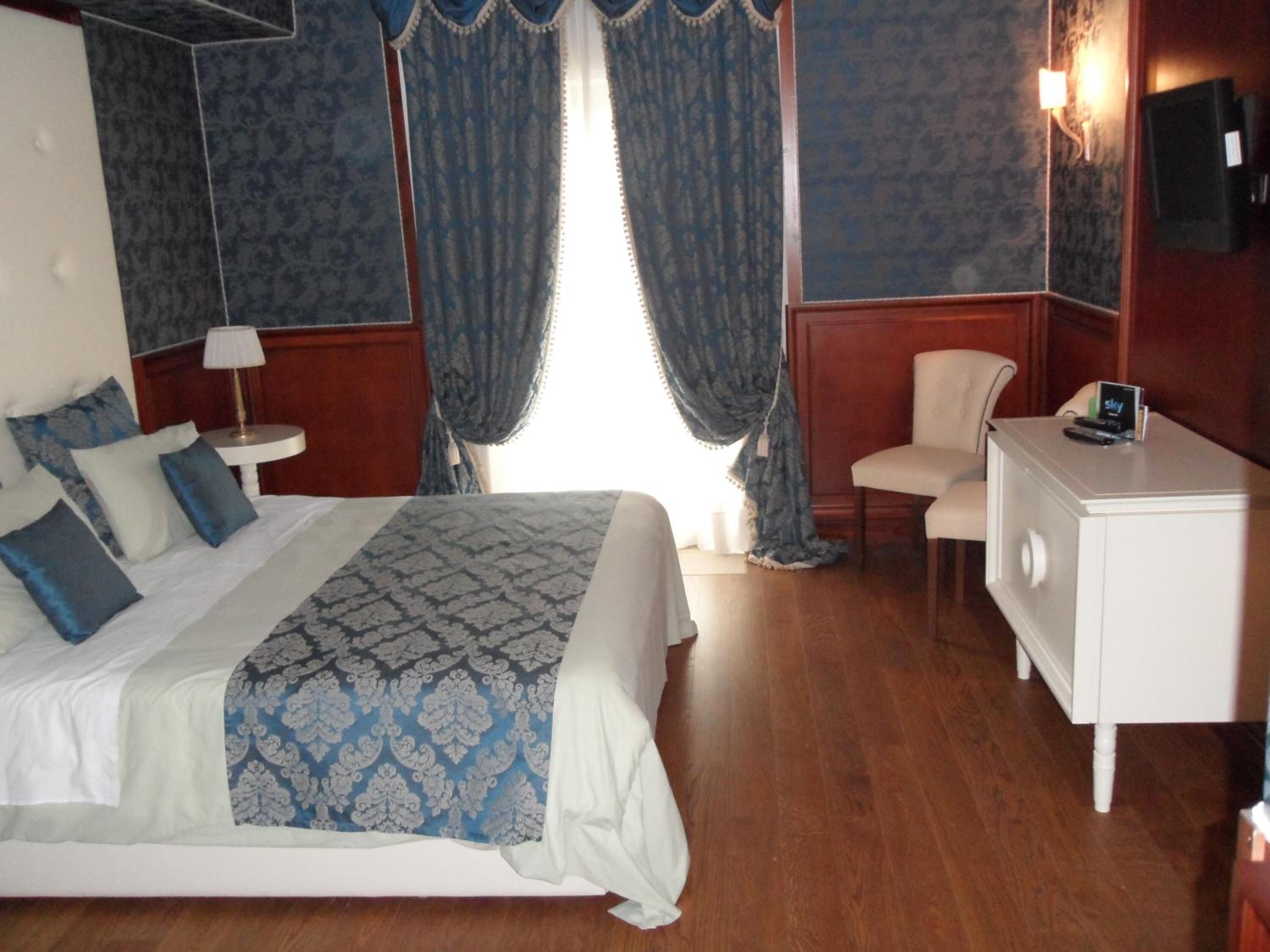 Quarto de hotel com uma cama, escrivaninha, cadeira, abajur e televisão.