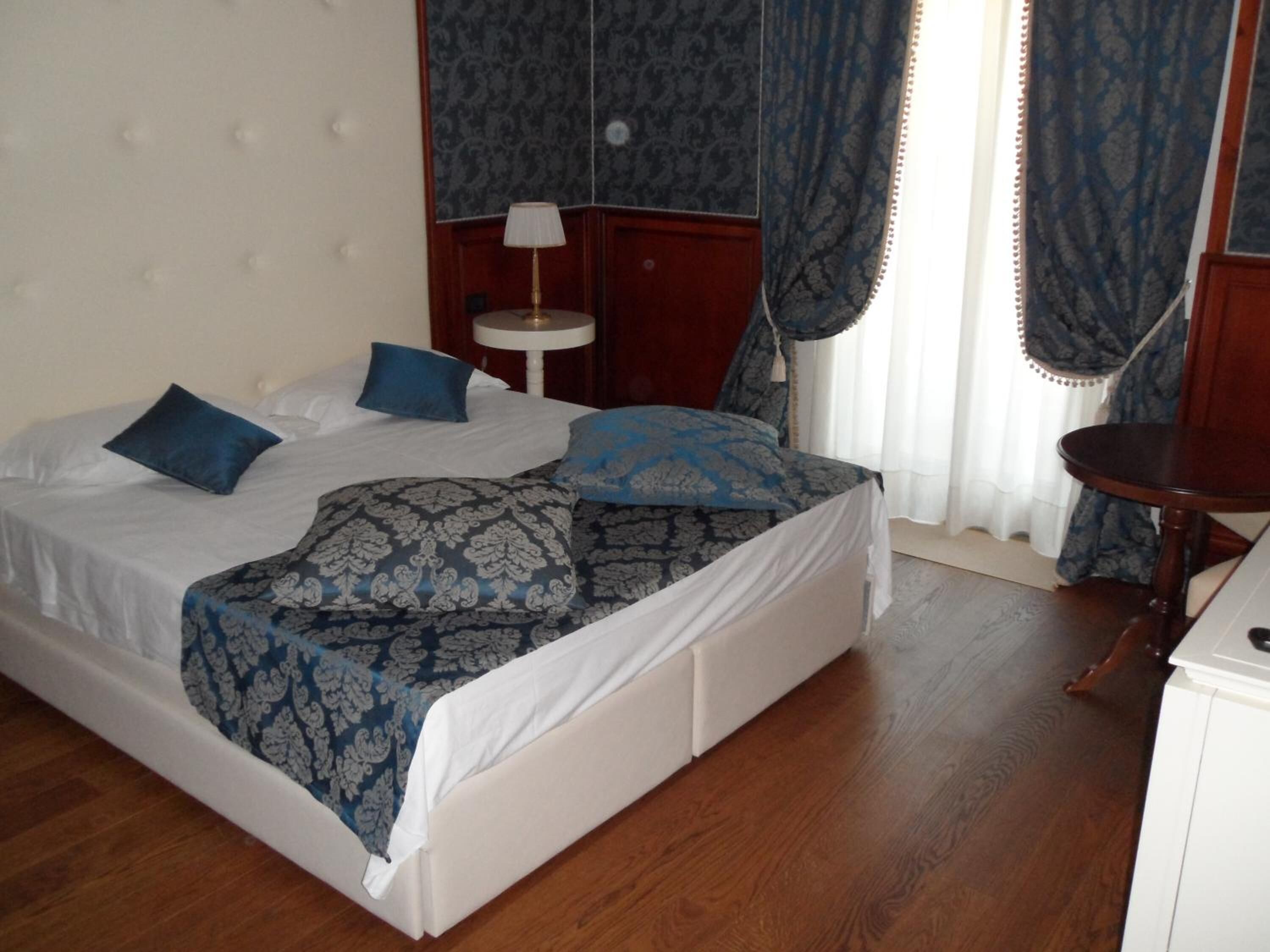 Una cama bien hecha con ropa de cama azul y blanca, una mesita de noche con una lámpara y un tocador de madera.