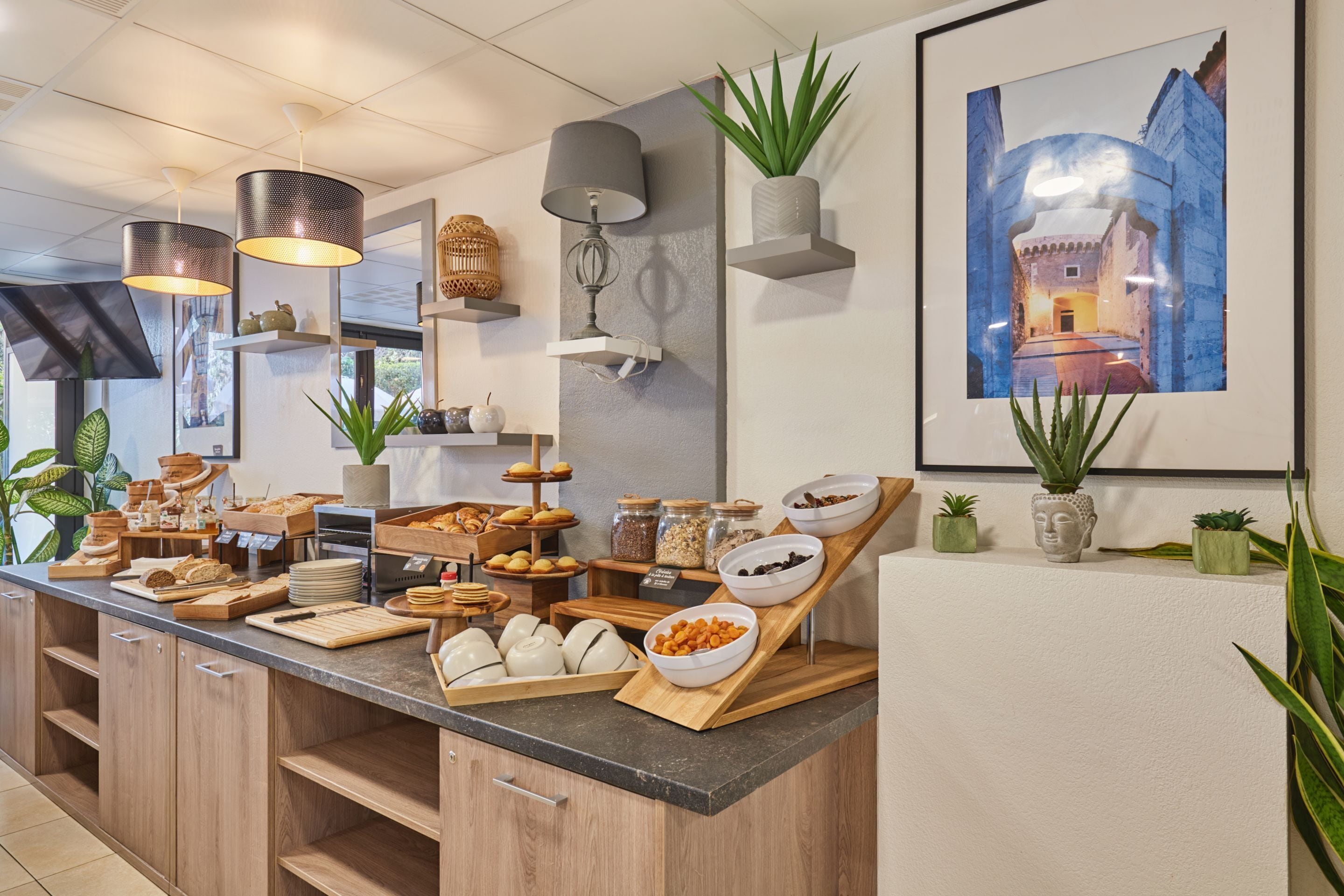 A breakfast buffet with various food items, a Buddha statue, and a framed painting on the wall.
