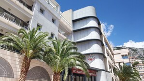 A multi-story hotel with a curved facade, palm trees in front, and a clear blue sky. - Appart'hôtel Odalys City - Monaco Les Hauts de la Principauté (Beausoleil)