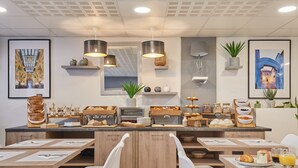 A breakfast buffet with various food items, wooden tables, white chairs, and hanging pendant lights. - Appart'hôtel Odalys City - Monaco Les Hauts de la Principauté (Beausoleil)