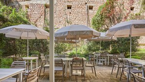 An outdoor dining area with tables and chairs, umbrellas, and a stone building in the background. - Appart'hôtel Odalys City - Monaco Les Hauts de la Principauté (Beausoleil)