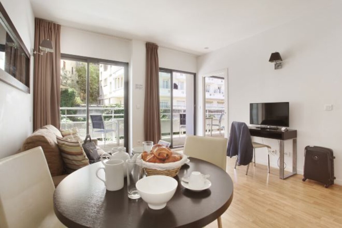 A modern living room with a round dining table, a sofa, a television, and a balcony view.