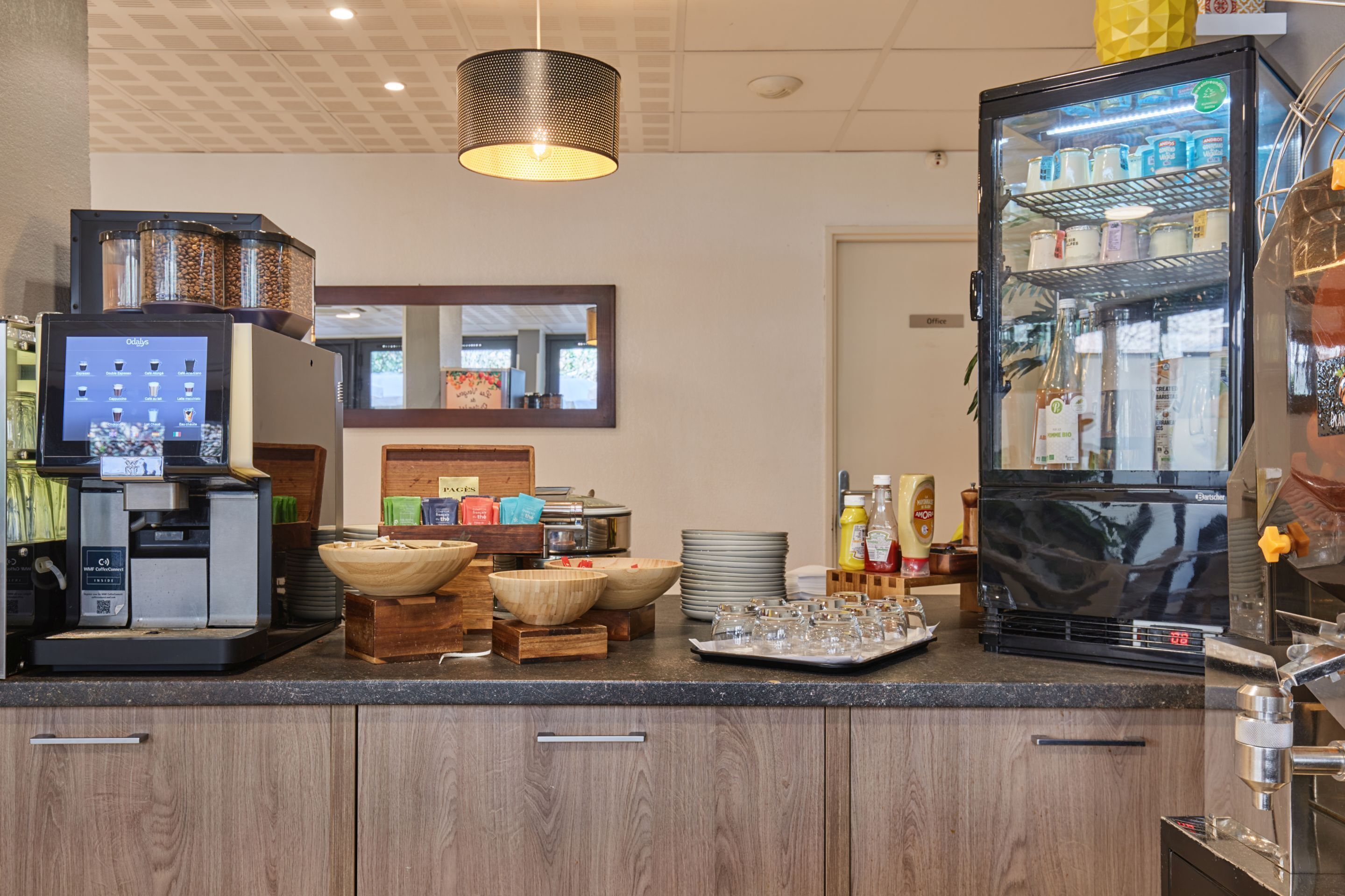 A kitchen area with a coffee machine, a beverage dispenser, and a refrigerator stocked with beverages.