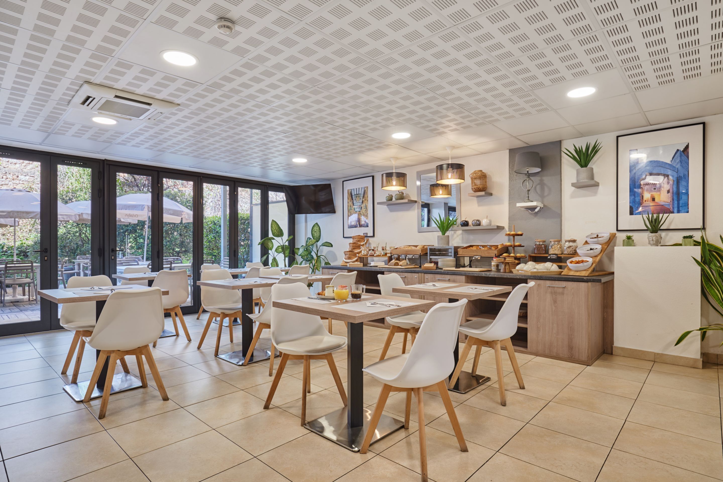 Ein modernes Café mit Innenbestuhlung, einer Theke mit Lebensmittelauslagen und großen Fenstern mit Blick ins Freie.