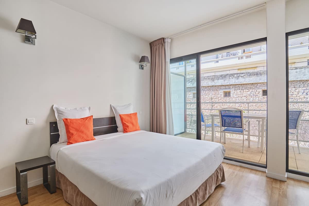 Une chambre d’hôtel moderne dotée d’un grand lit, d’une petite table, d’un balcon avec coin salon extérieur et offrant une vue sur la ville.