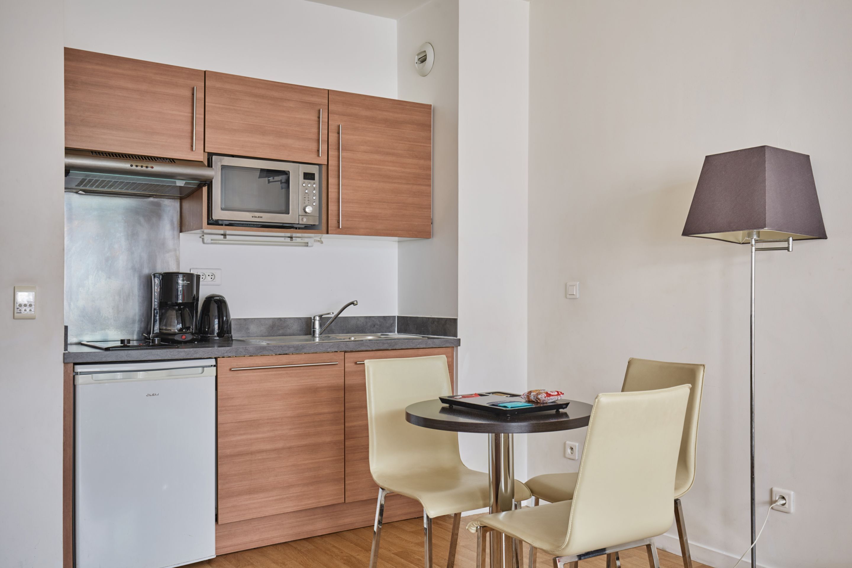 A compact kitchen with a microwave, coffee maker, and a dishwasher. There are two chairs around a small table.