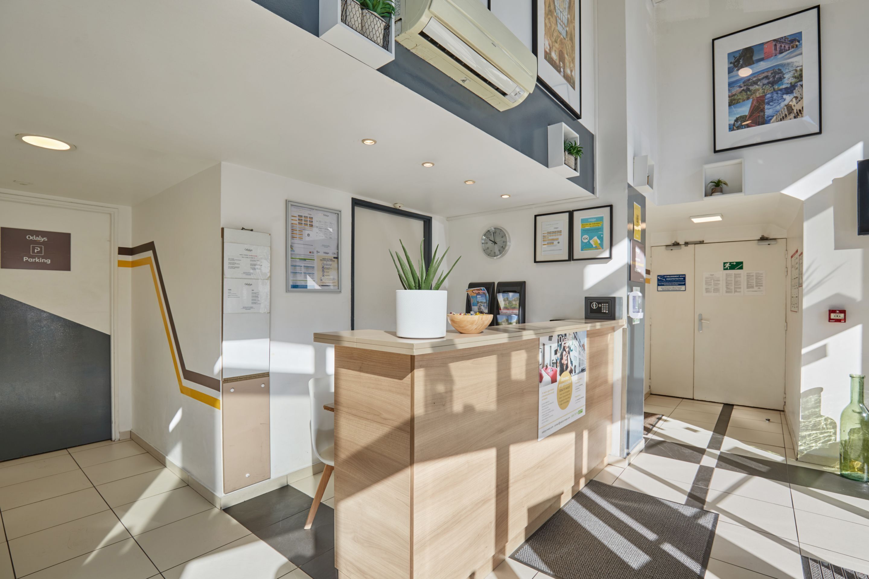 A reception desk with a plant, framed pictures, and a clock on the wall.