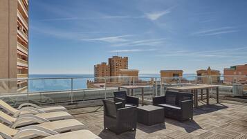 Terraza en la azotea con sillones de descanso, una mesa y vistas al mar y edificios.