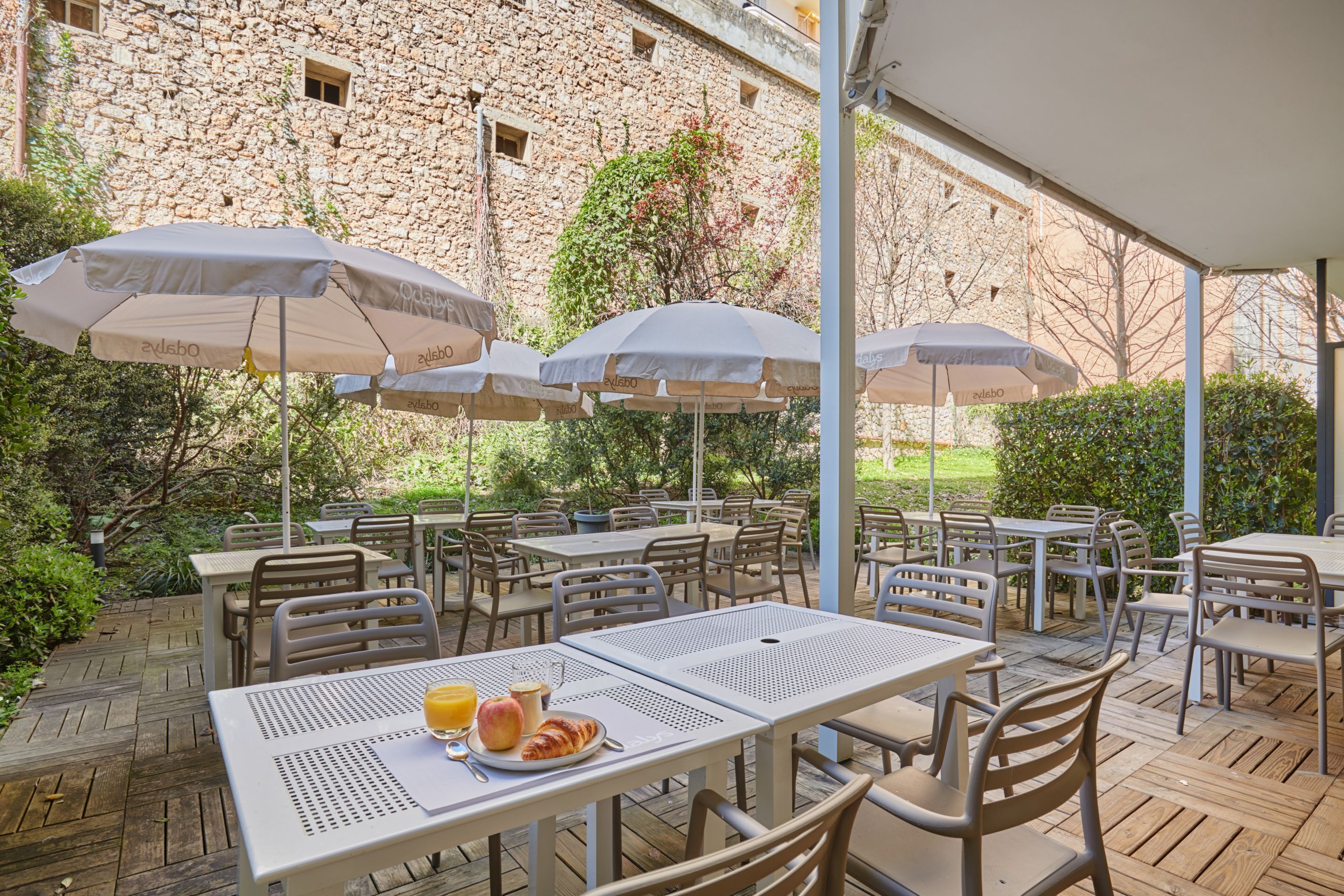 Une terrasse extérieure avec des tables et des chaises, des parasols, et un bâtiment en pierre en arrière-plan.