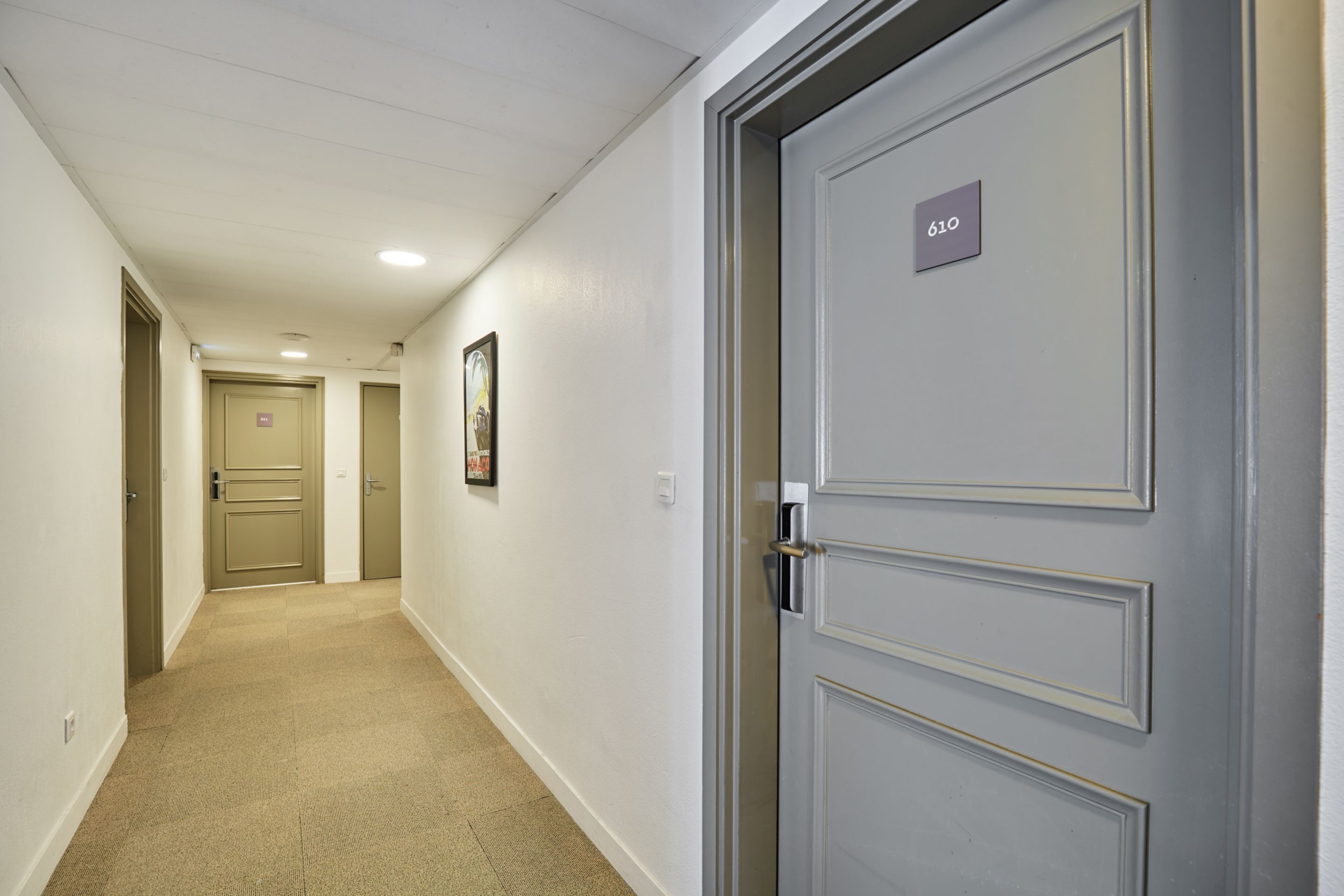 Un couloir avec un tapis beige, des murs blancs et des portes numérotées 610 et 611.