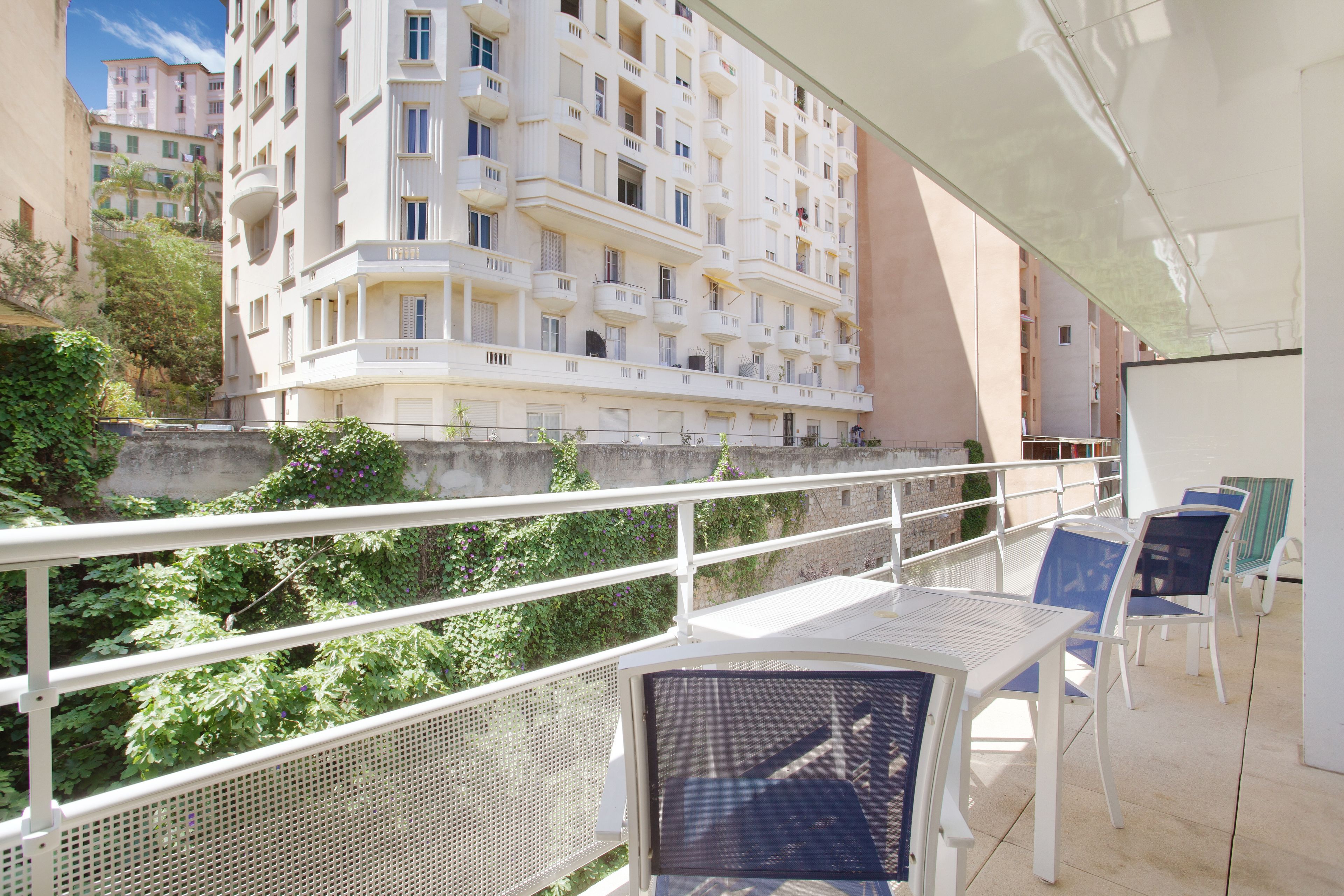 An outdoor balcony with white metal railings, a table, and blue chairs.