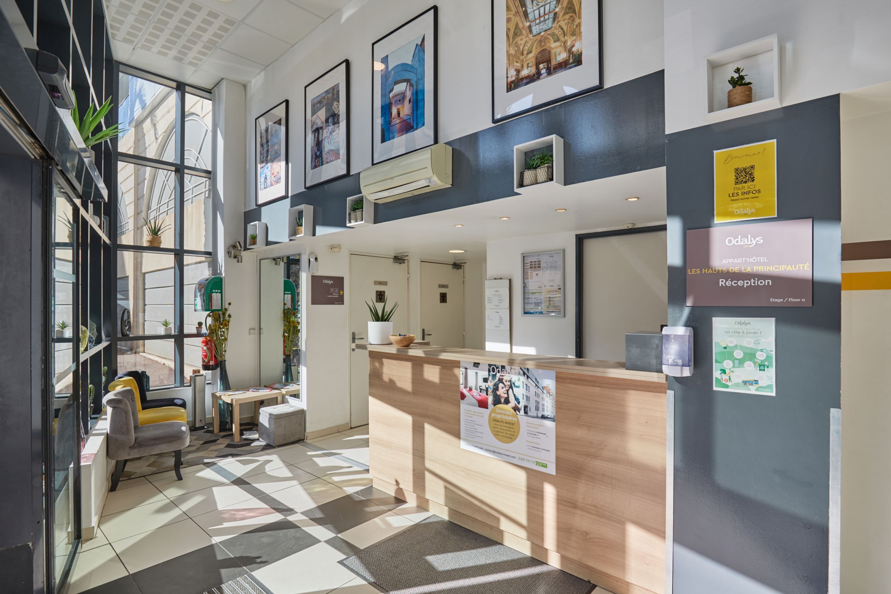A hotel reception area with a reception desk, seating area, and framed artwork on the walls.
