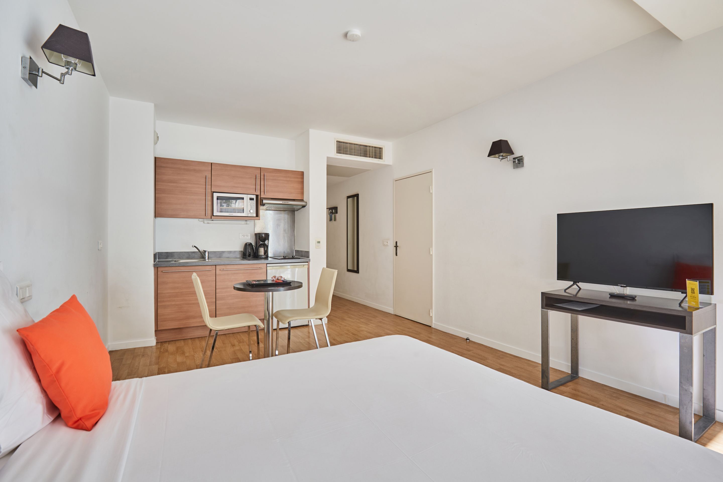 Ein Hotelzimmer mit Bett, Schreibtisch, Fernseher, einer Küchenzeile und einem Sessel.