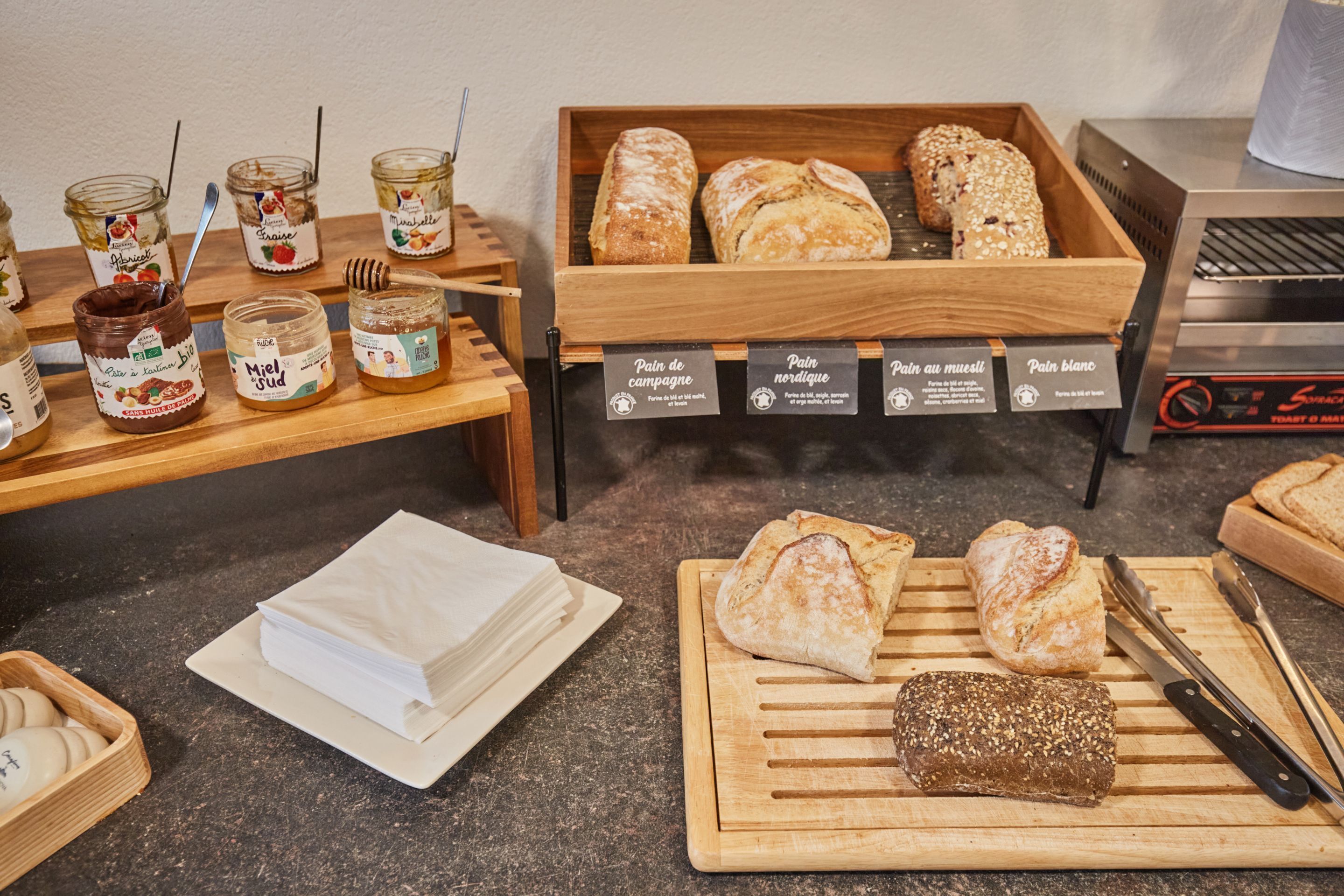 A bakery display with various types of bread and jars of spreads.