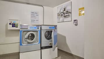 A laundry area with two front-loading washing machines, a price sign, a small control panel, and a framed picture on the wall.