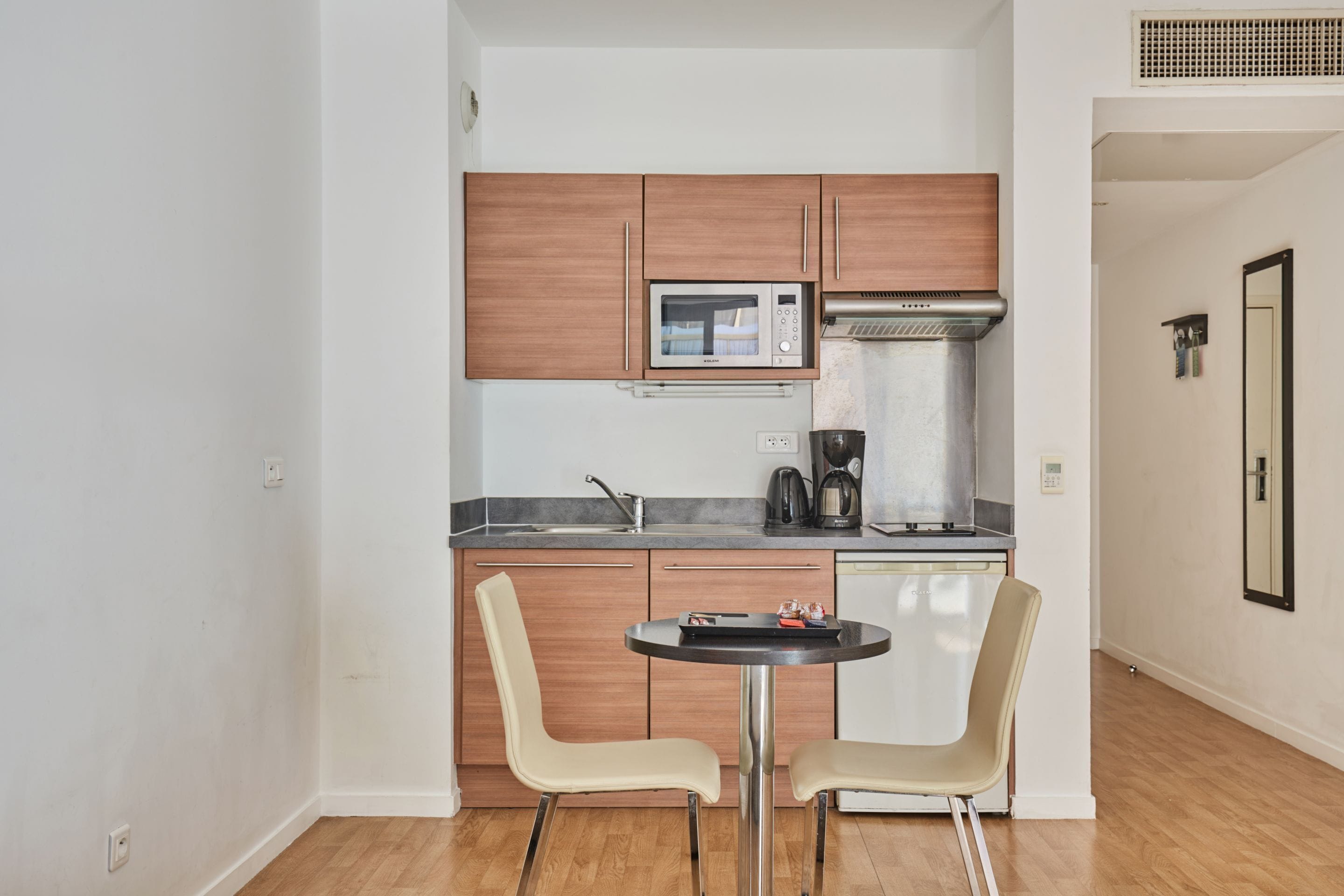 A compact kitchen with wooden cabinets, a microwave, a coffee maker, and a small dining table with two chairs.