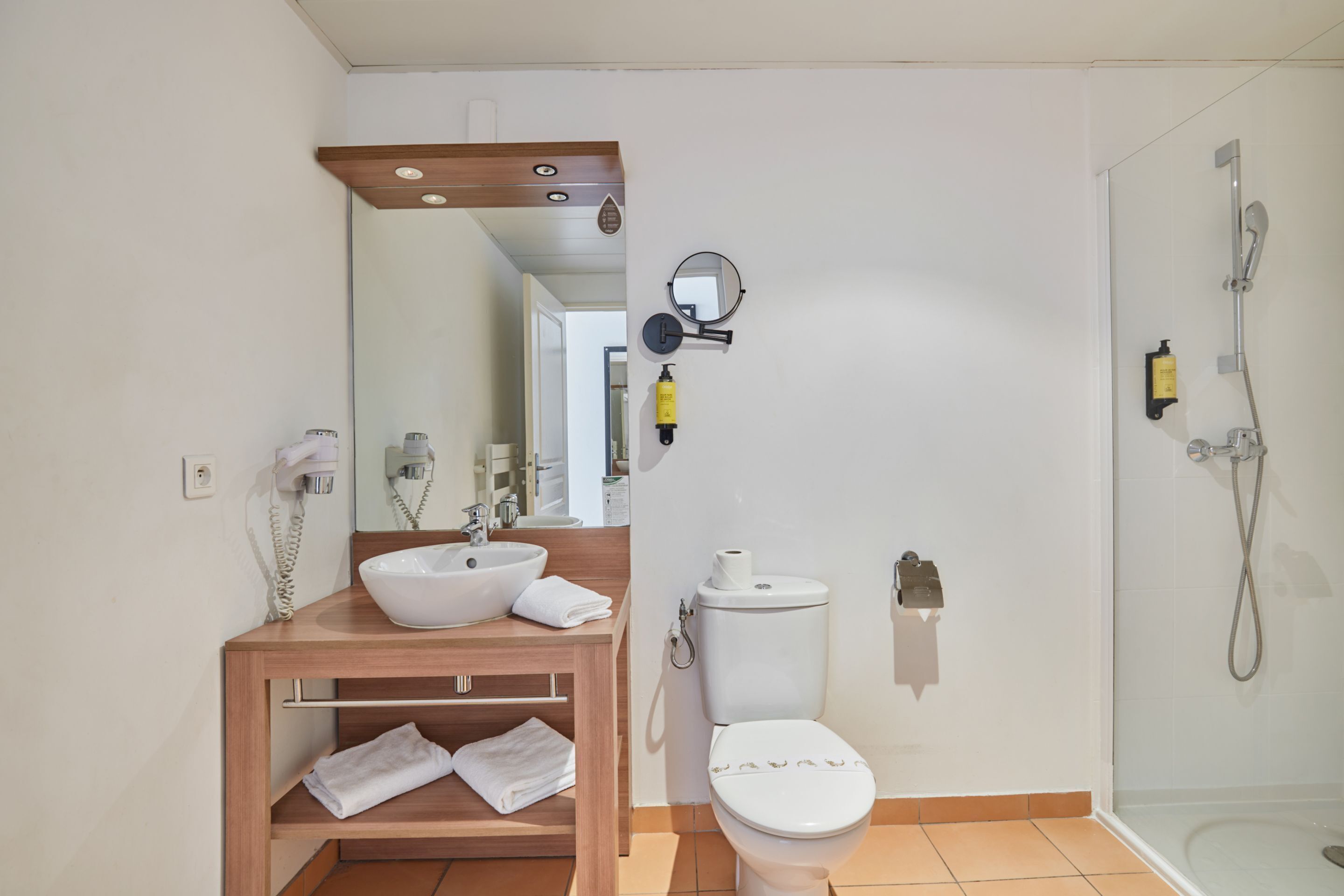 Une salle de bain avec un meuble-lavabo en bois, un lavabo blanc, des toilettes et une douche à parois de verre.