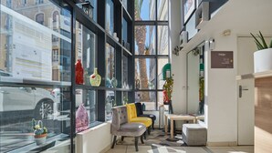 A modern hotel lobby with a glass wall, a seating area with a sofa and armchairs, a reception desk, and a sign for Odalys parking. - Appart'hôtel Odalys City - Monaco Les Hauts de la Principauté (Beausoleil)