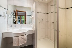 Ein modernes Badezimmer mit einer gläsernen Duschkabine, einem großen Waschbecken mit Spiegel und einem Handtuchhalter.