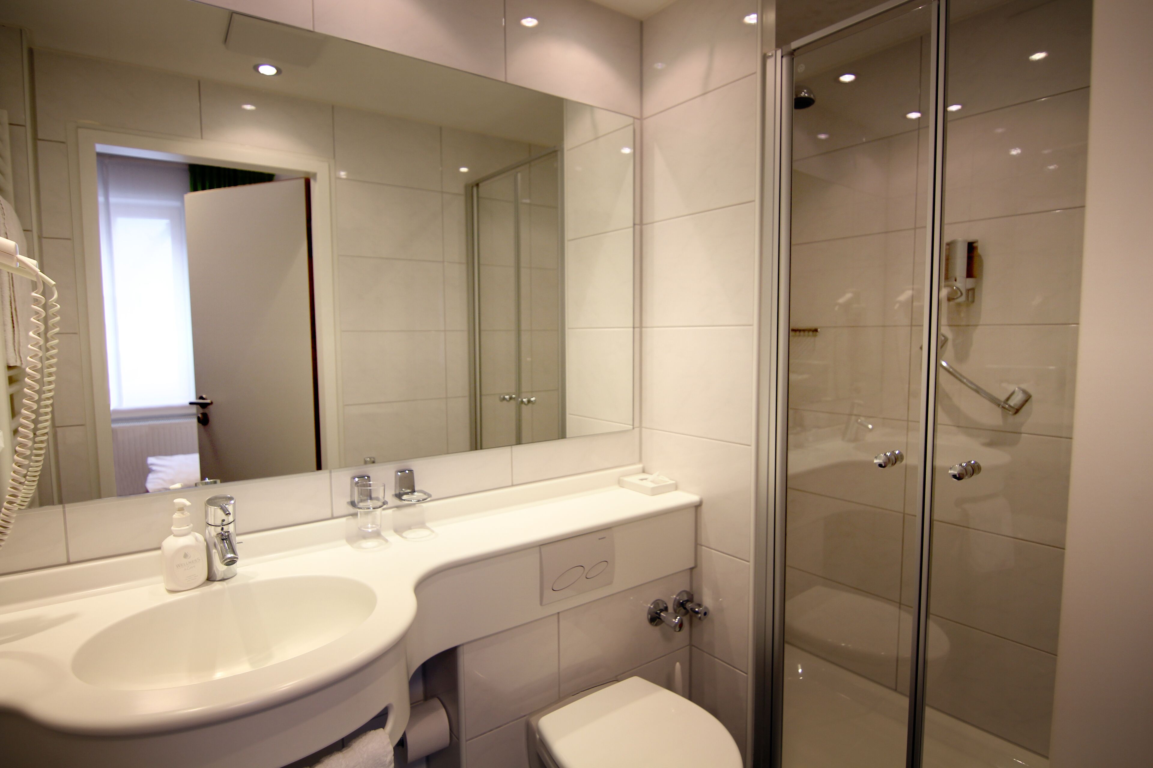 A modern bathroom with a large mirror, a sink, a toilet, and a glass-enclosed shower.
