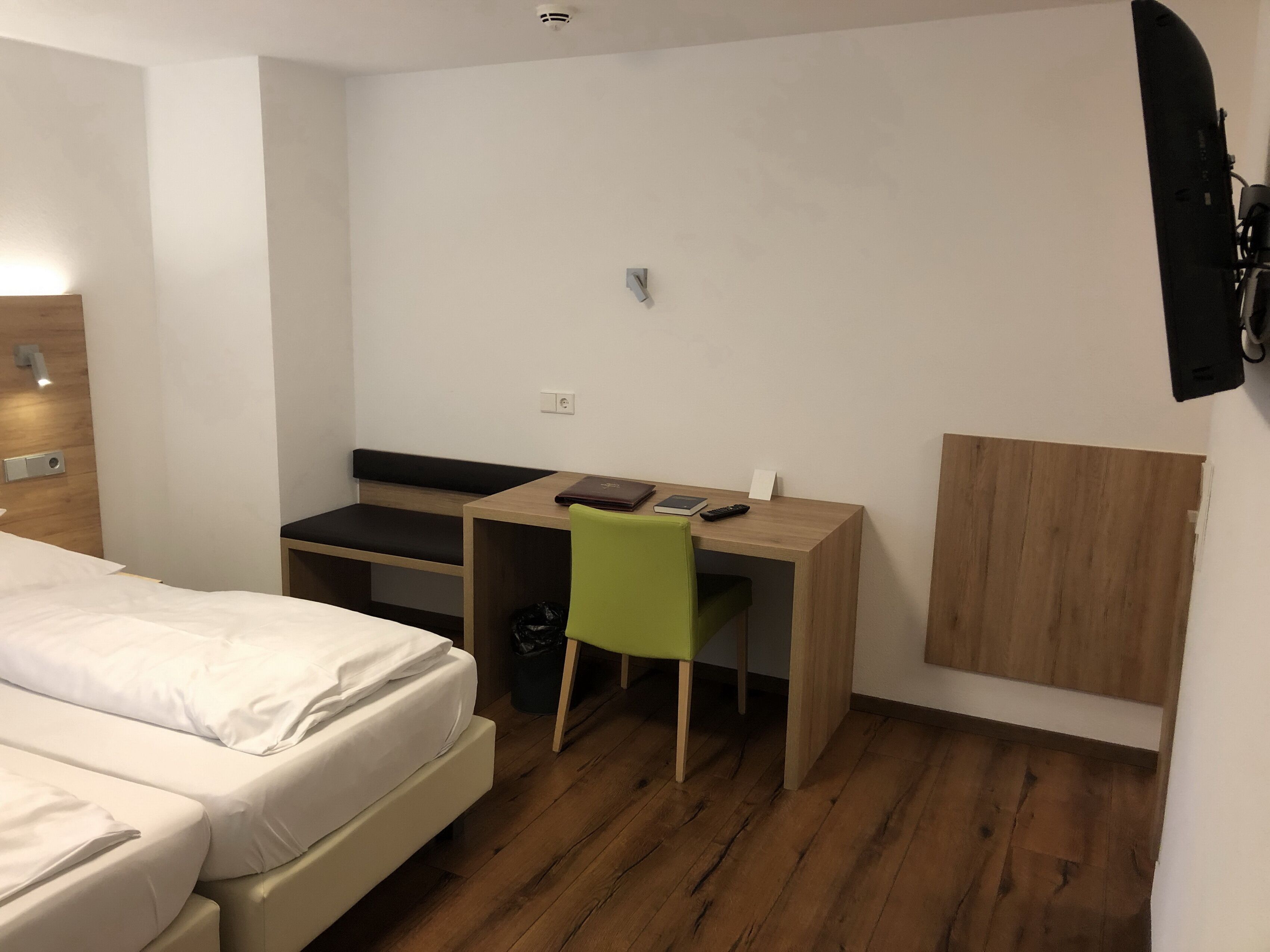 A hotel room with a bed, a desk, a chair, and a TV mounted on the wall.