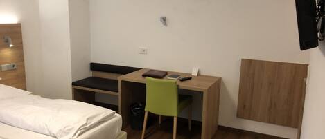 A hotel room with a bed, a desk, a chair, and a TV mounted on the wall.