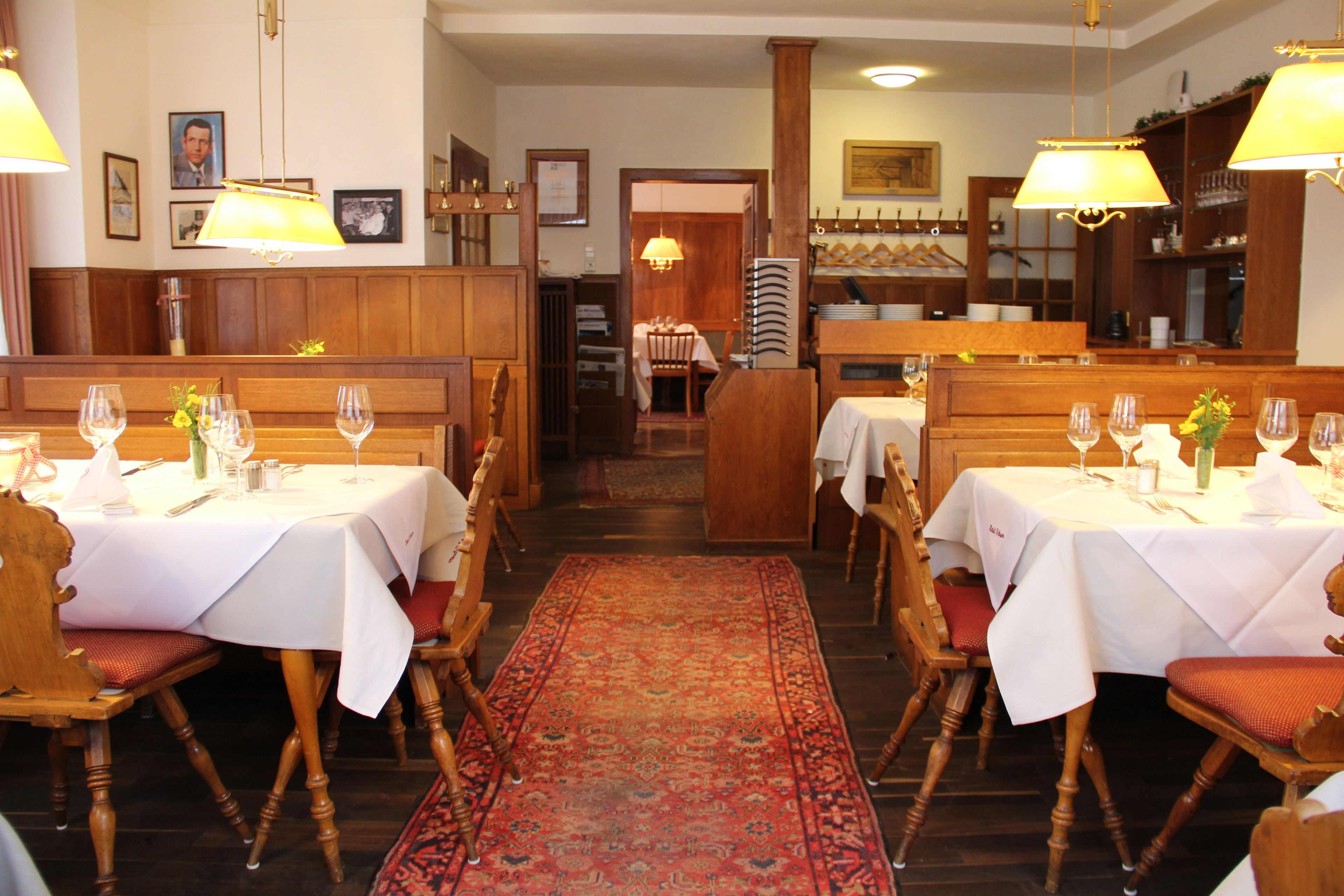 Un restaurante con cabinas y mesas de madera, alfombra roja estampada y lámparas colgantes.