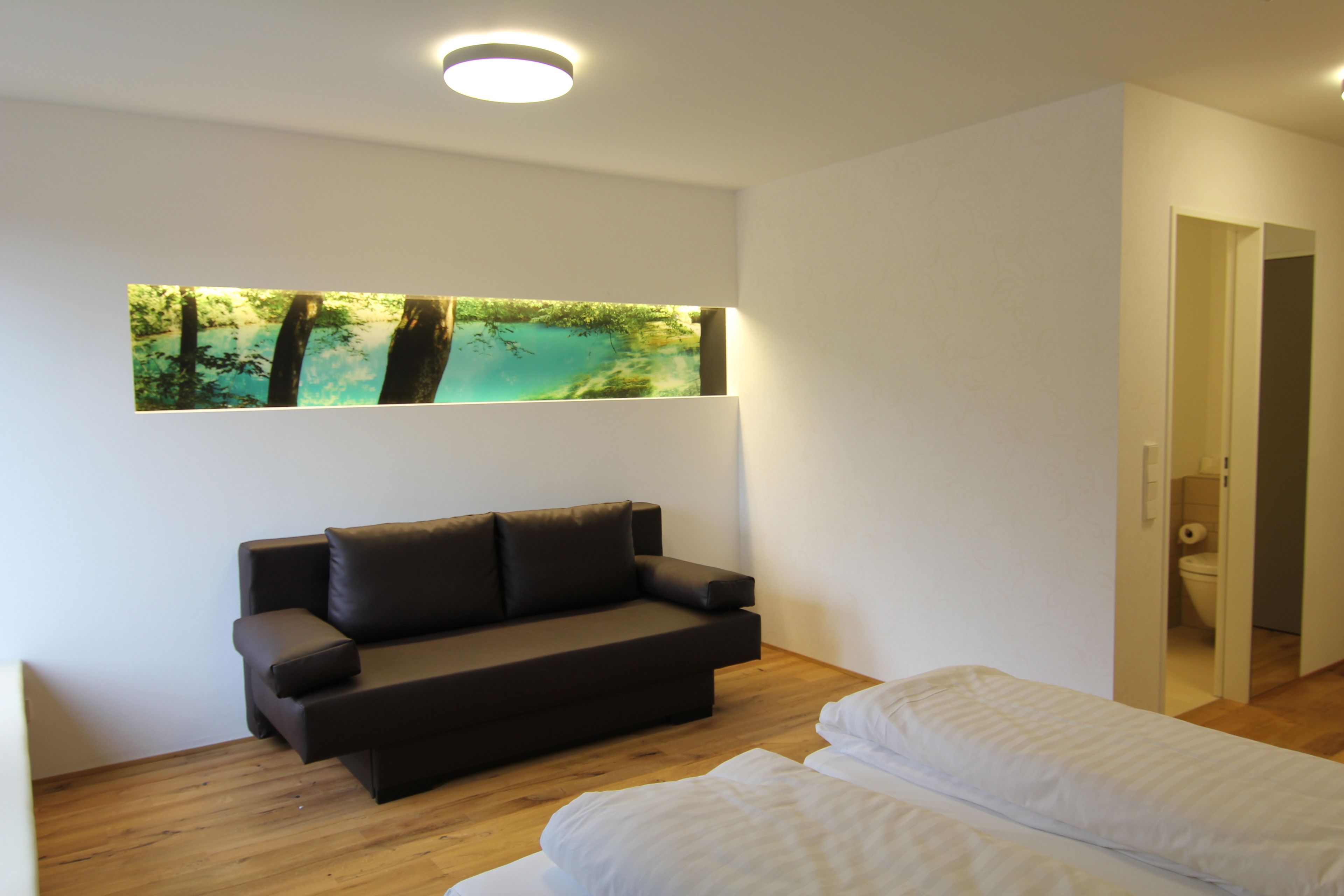 Una habitación moderna con sofá, cama y un cuadro de un paisaje forestal en la pared.