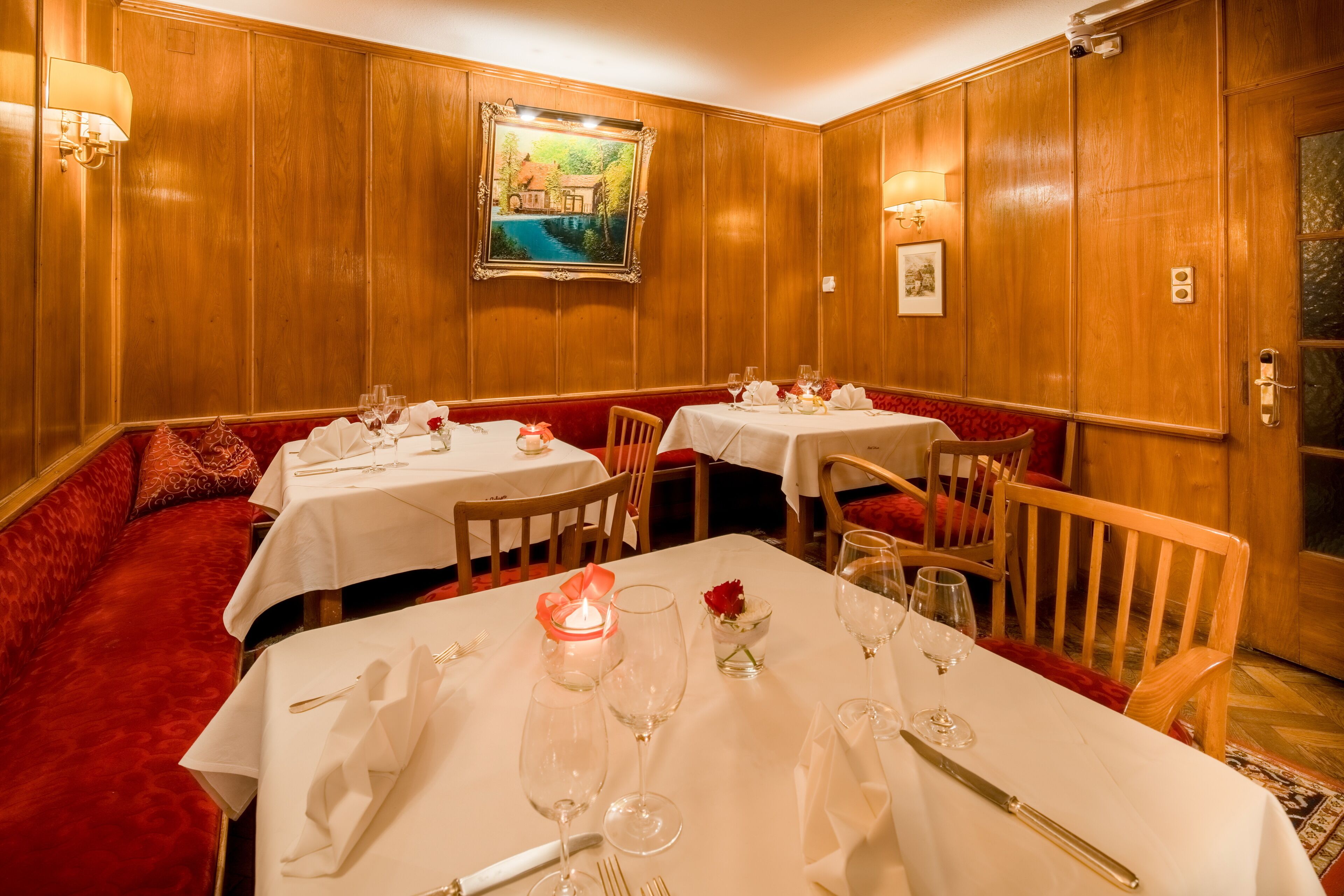 Un espace repas avec des lambris en bois, des sièges rembourrés de couleur rouge et des tables recouvertes de nappes blanches, ainsi que des verres à vin.