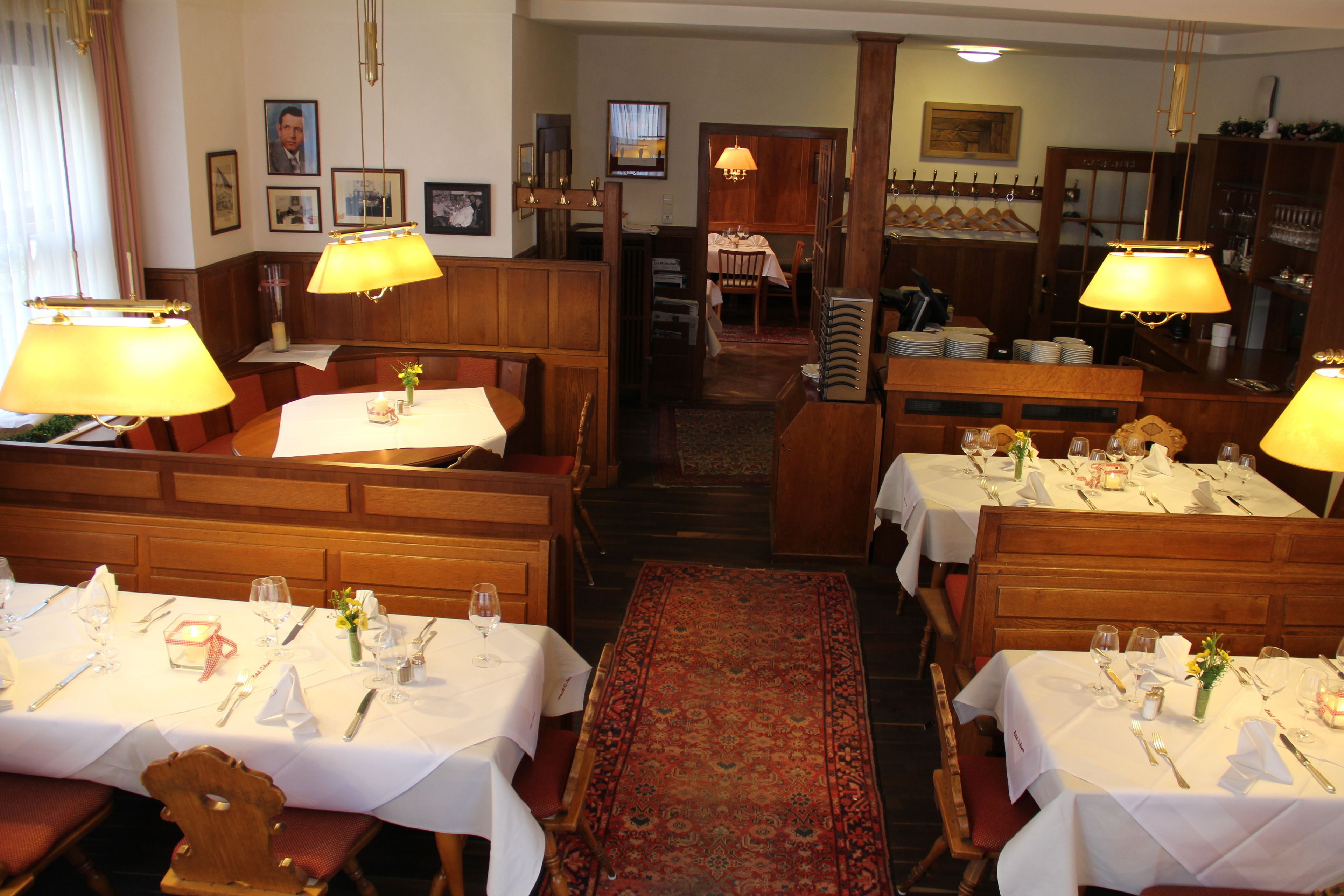 Un restaurante con cabinas y mesas de madera, cada conjunto con manteles blancos, copas de vino y cubiertos.