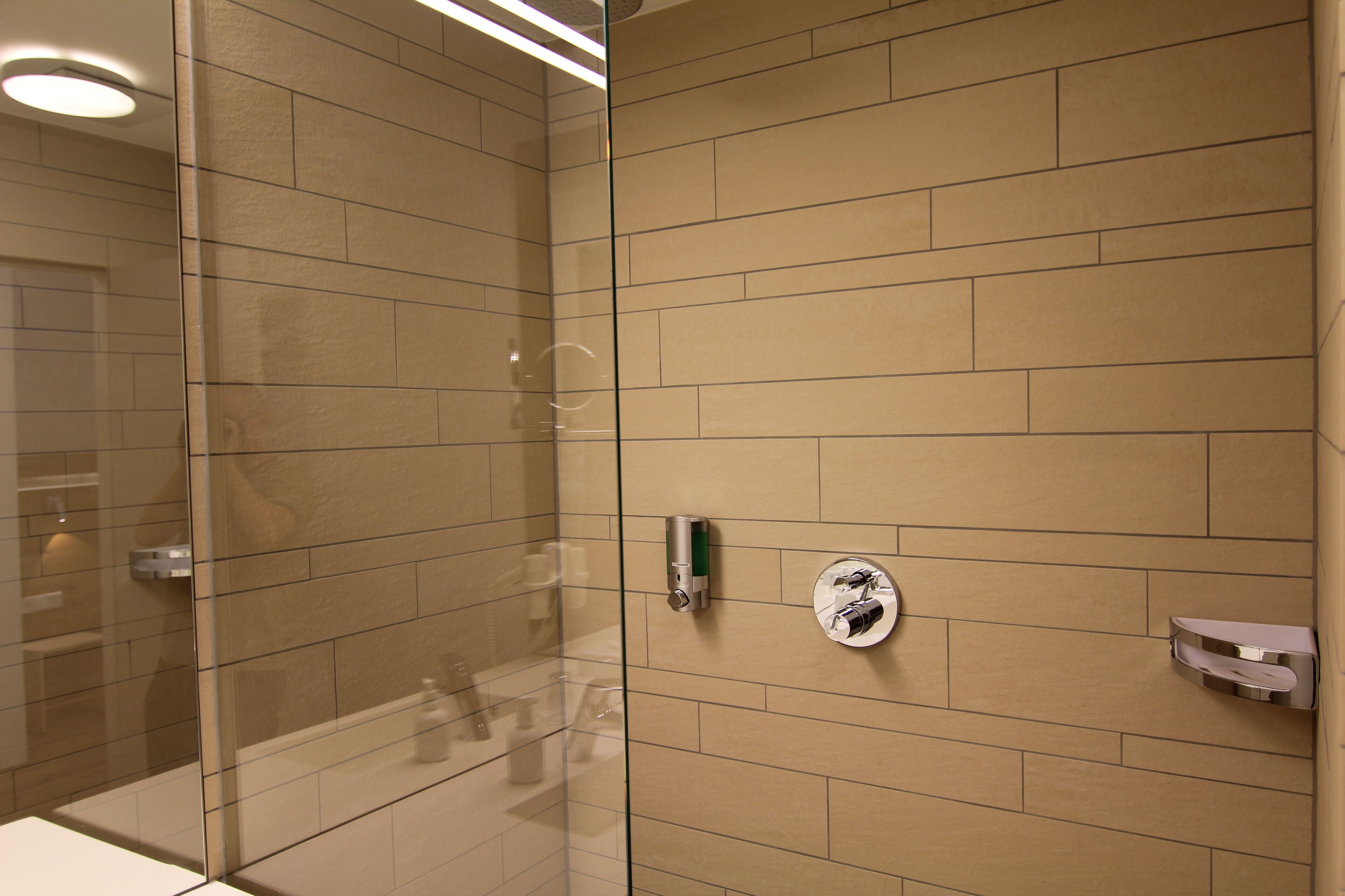Un baño moderno con cabina de ducha de vidrio, azulejos color beige y dispensador de toallas de pared.