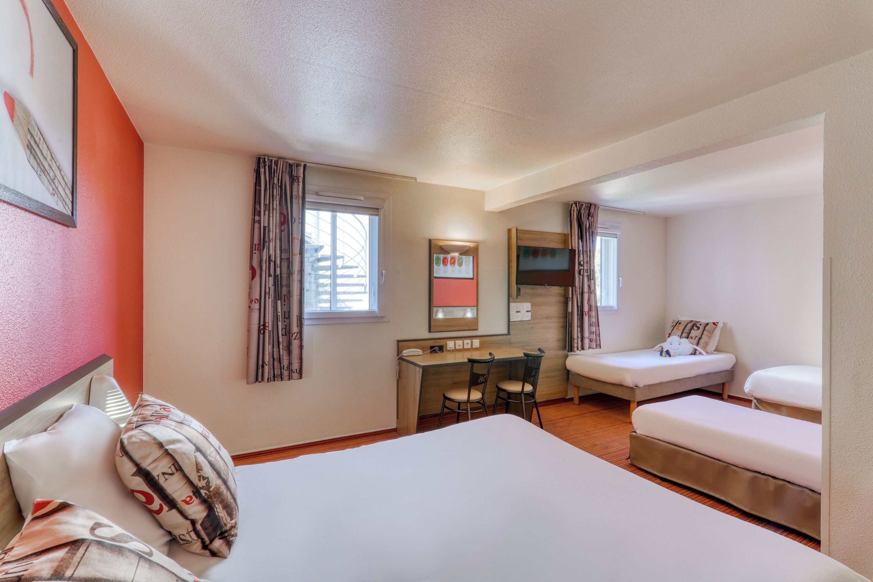 A hotel room with a bed, a desk, two chairs, a TV, and a small sofa.