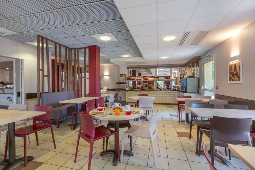 A cafeteria with tables and chairs, a counter with food items, and a kitchen area in the background.