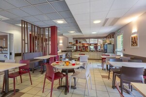 Una cafetería con mesas y sillas, una barra con alimentos y un área de cocina al fondo.