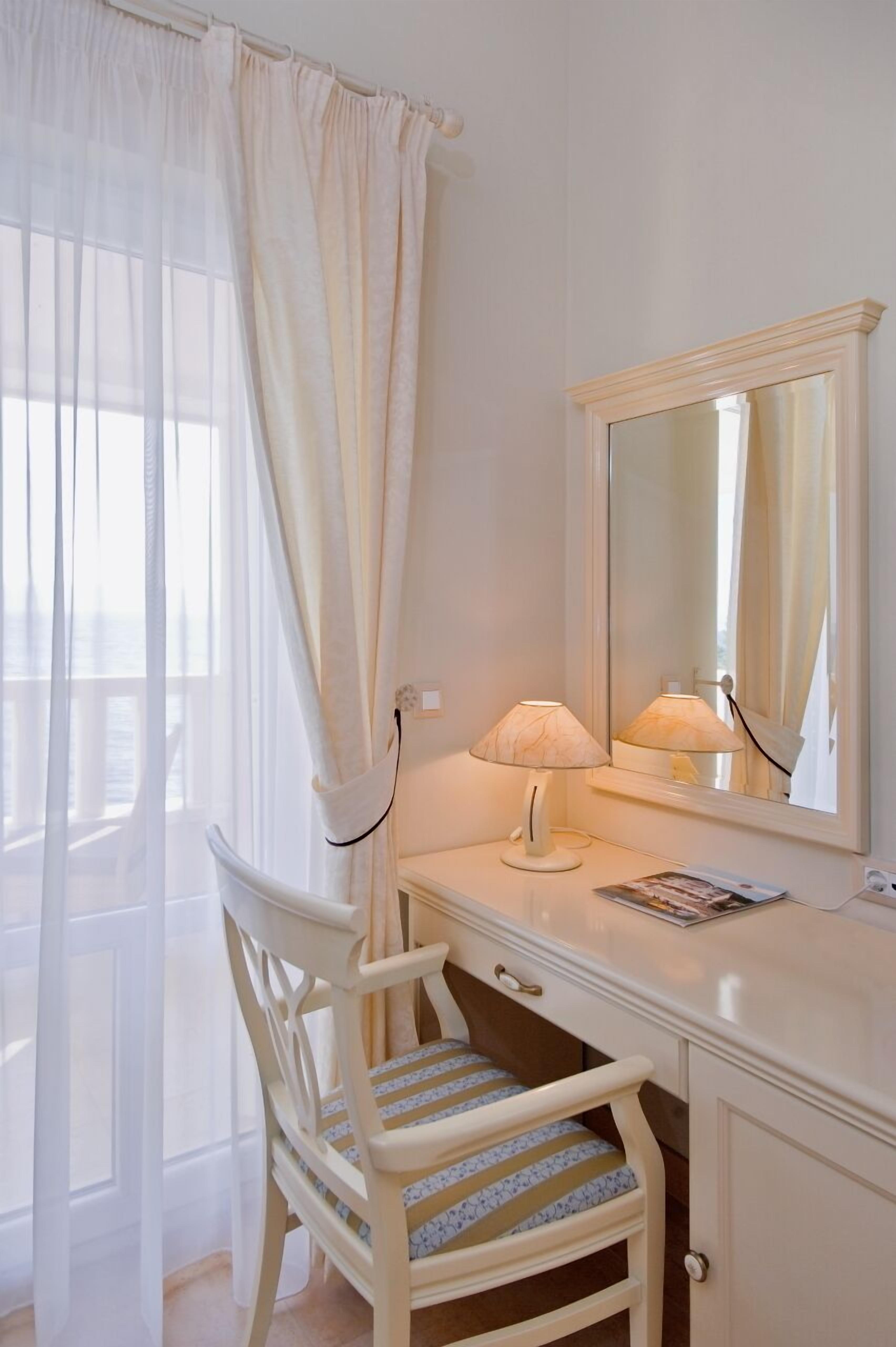 Une coiffeuse blanche avec un miroir, une chaise avec un coussin à rayures et une lampe.