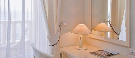 Une coiffeuse blanche avec un miroir, une chaise avec un coussin à rayures et une lampe.