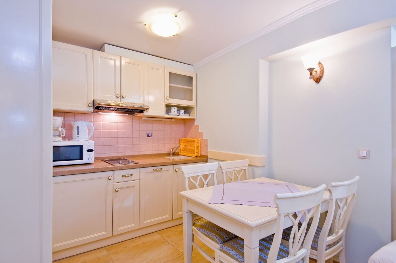 Une cuisine compacte avec des meubles blancs, un four à micro-ondes et une petite table à manger avec des chaises.